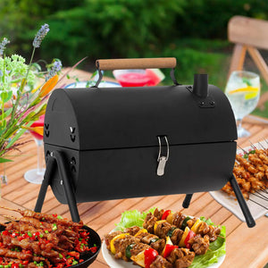 Black portable barbecue grill on a wooden table with food and drinks in the background