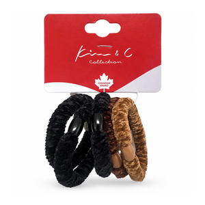 Three plush hair ties from the Kim & C Collection, featuring black, dark brown, and light brown faux fur textures with wooden beads, attached to a red cardboard hanger.