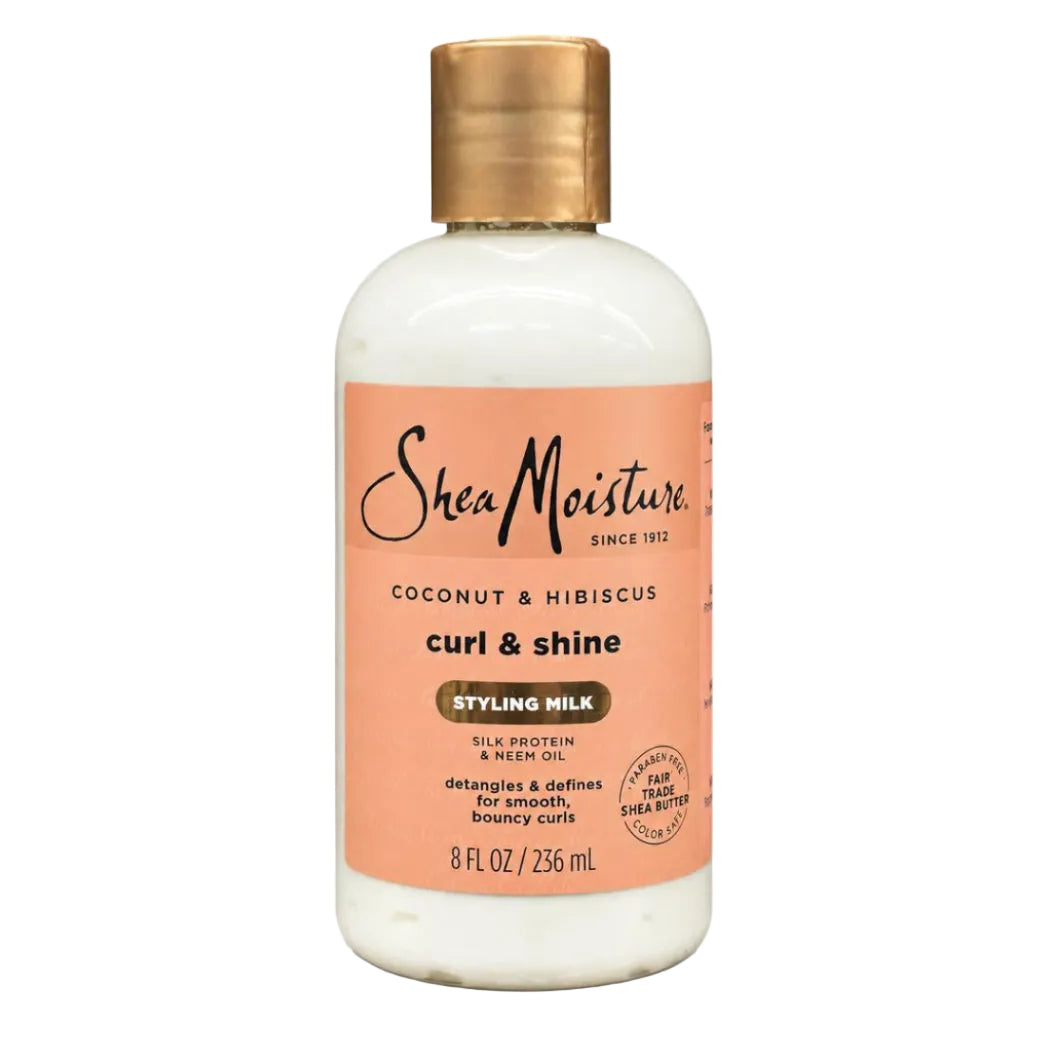 A bottle of SheaMoisture Curl & Shine Styling Milk in Coconut & Hibiscus, featuring an off-white bottle, a peach-colored label, and a metallic gold cap, set against a plain white background.