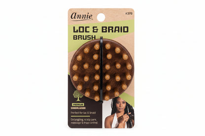 Annie Loc & Braid Brush in premium saffronwood, shown in its original retail blister packaging. The package features a brown cardboard backing with a green accent stripe, displaying the round wooden brush with its brown bristles.